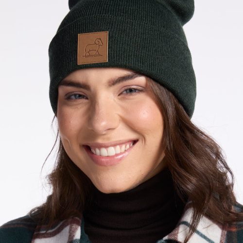 A woman wearing a Baylor Beanie - Pine by Woolx, crafted from cozy Merino Wool, smiles warmly for a picture.