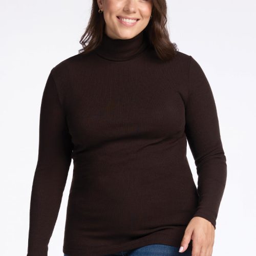 A person with long hair smiles while wearing the Sage Ribbed Turtleneck in French Roast from Woolx and blue jeans. The ribbed texture adds dimension, enhancing their casual look as they stand against a plain white background. | Juliana is 5'10", wearing a size XL