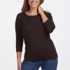 A person smiles while posing in a casual outfit, wearing the Woolx Jenny 3/4 Sleeve Crew Neck in French Roast and blue jeans. They have long hair and stand against a plain white background. | Jessie is 5'9", wearing a size S