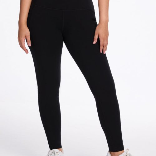 A person stands against a white background, wearing a black crop top, Woolx Frost Duralite® Leggings in black, and white sneakers. The image focuses on their midsection and legs, showcasing a casual and sporty outfit. | Sarah is 5'8", wearing a size S