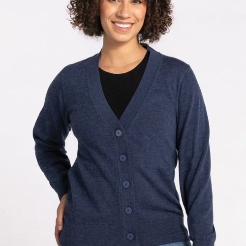 A smiling person with curly hair is wearing the Gia Sweater - Twilight Storm from Woolx over a black shirt and light blue jeans, standing against a plain white background. | Tori is 5'7", wearing a size S