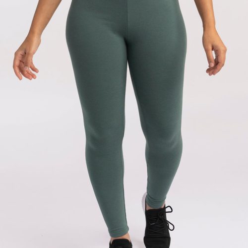 A person wearing Woolx Stella leggings in duck green and black sneakers stands against a plain background. Their arms are slightly bent at the elbows, and their hands hang relaxed by their sides.