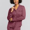 A person with curly hair smiles while wearing the Harper FeatherTouch® Pajama Set in Wild Ginger from Woolx, crafted from soft Merino wool. They are standing against a plain gray background.