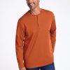 A man with short, graying hair smiles while wearing the Woolx Jackson Henley in Cinnamon Stick and blue jeans. He stands with his hands in his pockets against a plain white background. | Matthew is 6’, wearing a size L