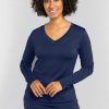 A person with curly hair is smiling, dressed in a long-sleeve Lily V Neck Lounge Top and matching pants by Woolx, both in the color Starry Night and made from moisture-wicking Merino wool. They stand against a plain light gray background.