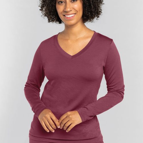 A person with curly hair smiles while wearing the cozy Lily V Neck Lounge Top in Wild Ginger from Woolx, paired with matching pants. The background is a light gray. | Tori is 5'7", wearing a size S