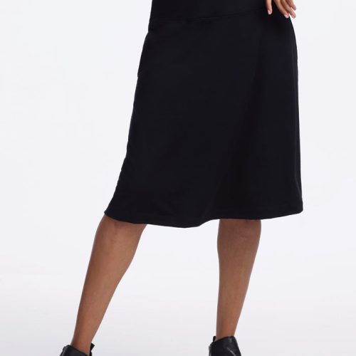 A person wearing a blue long-sleeve top and the Woolx Marilyn Flowy Midi Skirt - Black stands confidently in black ankle boots, one hand on their hip.