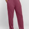 The person is dressed in Woolx Maya Lounge Pants in Wild Ginger, made from lightweight fabric and highlighted by a white waistband. These relaxed-fit pants flow comfortably as the individual stands barefoot with one hand in the pocket against a simple background. | Tori is 5'7", wearing a size S