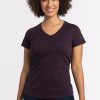 A person with curly hair smiles while standing against a plain background. They are wearing the Woolx Mia V Neck in Deep Plum, a stylish merino wool shirt that's odor-free, paired with dark jeans. | Tori is 5'7", wearing a size S