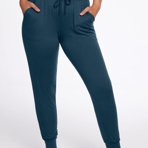 A person is wearing Woolx Mary Kate Lounge Pants in the Enchanted Forest color, with hands in pockets. These moisture-wicking pants feature an elastic waistband with a drawstring for added comfort. The person is barefoot, standing against a plain white background.