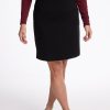 A person in a burgundy long-sleeve top and the elegant Woolx Monroe Knee Length Skirt in black stands against a plain white background. They are wearing black pointed-toe shoes, with their hands relaxed by their sides. | Andrea is 5’9”, wearing a size S