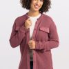 A person with curly hair smiles while wearing an Oaklynn Waffle Shacket in Wild Ginger from Woolx over a white shirt and blue jeans. They stand against a plain white background. | Tori is 5'7", wearing a size S