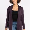 A person with curly hair smiles while wearing the Woolx Paisley Cardigan in Deep Plum, crafted from Australian Merino Wool, over a black top and blue jeans. They stand against a plain white background. | Tori is 5'7", wearing a size S