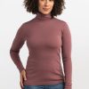 A person with curly hair wearing a Wild Ginger Peyton Turtleneck from Woolx and blue jeans stands against a plain white background. They are facing the camera with a neutral expression and one hand on their hip, ready for any adventure. | Tori is 5'7", wearing a size S