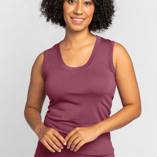 A person with curly hair is smiling, wearing the Phoebe Lounge Tank - Wild Ginger by Woolx, a maroon sleeveless top made of merino wool renowned for its cooling comfort, against a plain background. | Tori is 5'7", wearing a size S