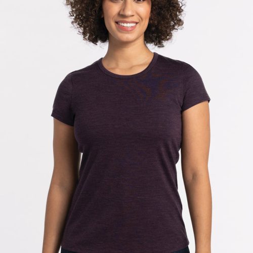 A person with curly hair is smiling while wearing the Woolx Addie Short Sleeve Crew in Deep Plum and dark jeans, standing against a plain white background. | Tori is 5'7", wearing a size S