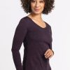 A person with curly hair smiles while wearing a long-sleeve Layla V Neck Top in Deep Plum by Woolx and jeans. They are standing against a plain white background. | Tori is 5'7", wearing a size S