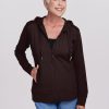 An older woman with short white hair smiles warmly as she wears the Woolx Ryann Hoodie in French Roast over a black top and blue jeans. With one hand in her pocket, she stands against a plain light gray background, exuding comfort and casual style. | Kathy is 5'9", wearing a size S