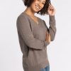 A person with curly hair smiles, wearing the Francesca Sweater in Sable from Woolx and blue jeans, standing against a plain white background. | Tori is 5'7", wearing a size S