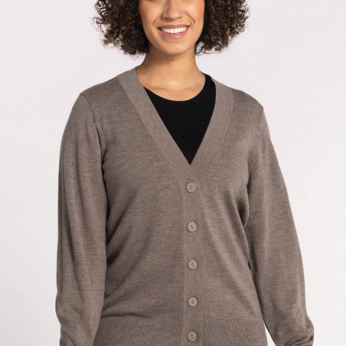 A person with curly hair smiles while wearing the Gia Sweater in Sable from Woolx over a black shirt and blue jeans, standing against a neutral background. This travel essential offers temperature-regulating comfort, making it perfect for any journey. | Tori is 5'7", wearing a size S