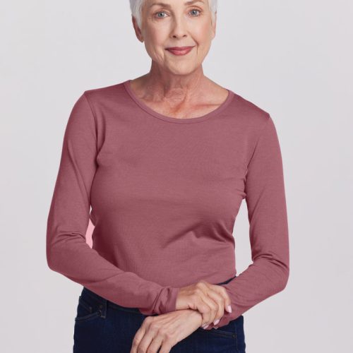 An older woman with short white hair is wearing the Woolx Remi Long Sleeve T-Shirt in Wild Ginger along with dark jeans, standing against a plain white background. She smiles gently and holds her hands together in front of her. | Kathy is 5'9", wearing a size S