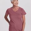 An older woman with short white hair smiles warmly, dressed in a Wild Ginger Mia V Neck by Woolx. She pairs it with blue jeans as she stands against a plain white background, her right hand confidently on her hip. | Kathy is 5'9", wearing a size S