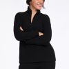 A person with dark hair smiles and gazes to the side while dressed in a black ribbed top and matching pants. With arms crossed in a relaxed manner against a plain white backdrop, they effortlessly exhibit the comfortable elegance of the Woolx Quinn Ribbed 1/4 Zip - Black. | Sarah is 5'8", wearing a size S