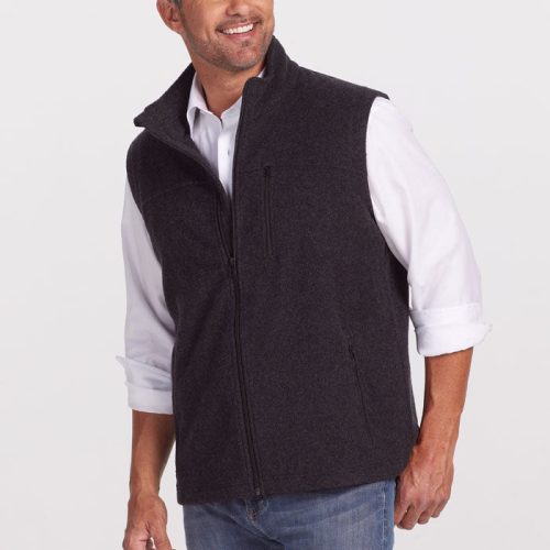 A man with short, dark hair is smiling and looking to the side. He is wearing a white button-up shirt with rolled-up sleeves and a warm Stowe Vest in Carbon Black by Woolx. He has on light blue jeans and is posed against a plain white background. | Matthew is 6', wearing a size L