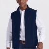 A person wearing a white button-down shirt, the Stowe Vest in Deep Navy from Woolx, blue jeans, and a brown belt stands against a plain light background. They have a neutral expression and one hand is slightly raised. | Trell is 6’2”, wearing a size M