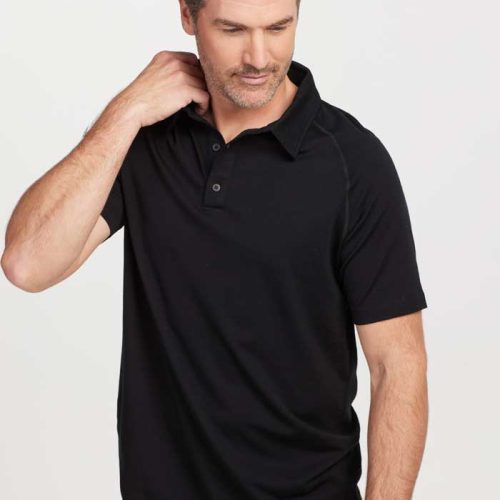 A man dressed in a sleek Summit Polo OLD by Woolx in black and blue jeans, designed with moisture management technology, touches his neck while looking down, standing against a white background.