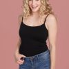 A person with curly blonde hair smiles while wearing the Woolx Teagen cami with built-in shelf bra and blue jeans, standing against a pink background.