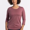 A person with curly hair is sporting a 3/4 sleeve, Wild Ginger Jenny Crew Neck by Woolx alongside dark jeans. They are standing against a plain white background and smiling gently. | Tori is 5'7", wearing a size S