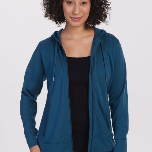 A person with curly hair is smiling at the camera against a plain backdrop, wearing the Ryann Hoodie in its athletic fit and real teal color by Woolx over a black top. | Tori is 5'7", wearing a size S