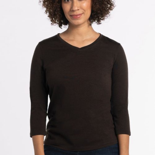 A person with curly hair is wearing a Woolx Elena V Neck in French Roast and dark jeans, standing against a plain white background. | Tori is 5'7", wearing a size S