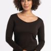 A person with curly hair is wearing the Woolx Layla V Neck Top in French Roast, a long-sleeve breezy knit shirt. They stand against a plain white background with a neutral expression. | Tori is 5'7", wearing a size S