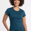 A person with curly hair is smiling while wearing a Woolx Addie Short Sleeve Crew in Real Teal, an odor-free tee crafted from Australian Merino Wool. They are standing against a plain white background. | Tori is 5'7", wearing a size S