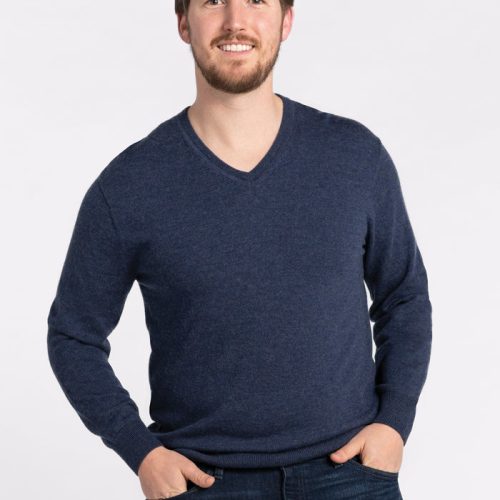 A man with a beard and short hair smiles at the camera, wearing the Vincenzo Sweater in Twilight Storm by Woolx along with dark jeans, standing against a plain white background with his hands in his pockets. | Will is 6', wearing a size M