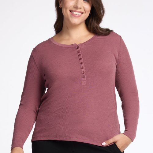 A person wearing a Reese Ribbed Henley in Wild Ginger from Woolx and black pants is smiling with one hand in their pocket, standing against a light gray background.