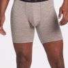 A person is wearing Woolx's Jazzy No Fly Boxer Briefs in Light Mocha, featuring a lightweight design and a black waistband with "Woolx" printed on it, standing against a plain background. These merino wool boxers offer both comfort and style. Their arms are relaxed by their sides.