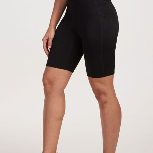 A person wearing a black sports top and the MERINO FLEX™ Dani Bike Shorts from Woolx, which are high-waisted and feature side pockets, is standing sideways. These bike shorts are made from Merino Flex Fabric for ultimate comfort. The individual also sports black athletic shoes with white soles, set against a plain, light-colored background. | Tori is 5'7", wearing a size S