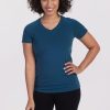 A person with curly hair is smiling, wearing the 'Mia V Neck' in Real Teal by Woolx and black pants. They stand against a plain white background, confident in their odor-free style. | Tori is 5'7", wearing a size S