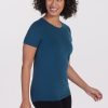 A person with curly hair, dressed in the Woolx Liza Crew Neck Tee in Real Teal and black pants, is smiling and looking to the side against a plain white background. | Tori is 5'7", wearing a size S