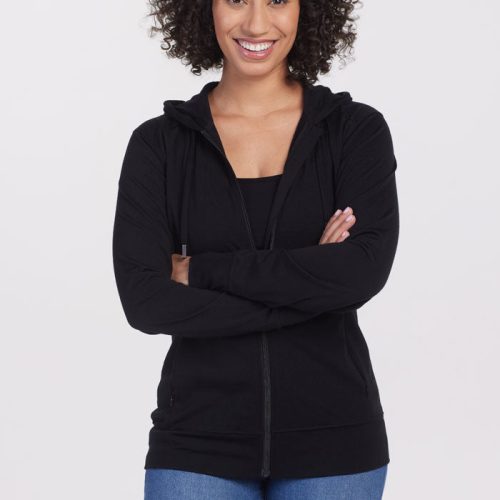 A person with curly hair stands smiling at the camera, wearing the lightweight Ryann Hoodie OLD in black by Woolx, paired with blue jeans, against a plain white background.