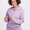 Dressed in a lilac Avery Hoodie from Woolx's Stocking Stuffer Final Sale Deals, a person beams with joy, their curly hair highlighting their smiling face as they hold the drawstrings. They stand confidently against a plain white background, radiating effortless style.