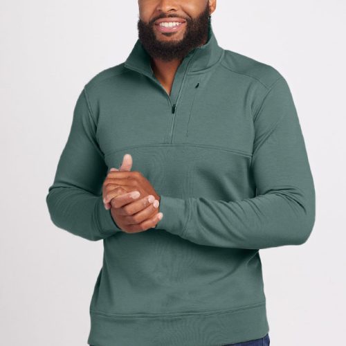 A man with a beard is smiling while wearing the Mason 1/4 Zip sweater from Woolx, crafted from odor-resistant Merino wool in Duck Green, paired with jeans. He stands against a plain background with his hands clasped together.