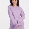 A person with long dark hair smiles while wearing a matching lilac Wool Aire™ Bailey set from Woolx, crafted from sustainable Merino wool. The background is plain white.