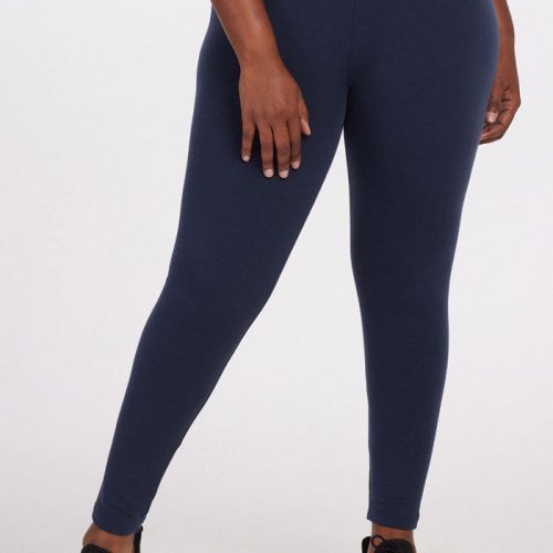 A person wearing the Deep Navy Stella Tall leggings by Woolx and black sneakers stands with one hand by their side. The plain white background accentuates the sleek design of these premium merino wool baselayer leggings.