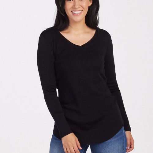 A person smiling, wrapped in the midweight warmth of a black Woolx Eva Tunic and blue jeans. They have luxuriously soft, long dark hair and are standing against a plain white background.