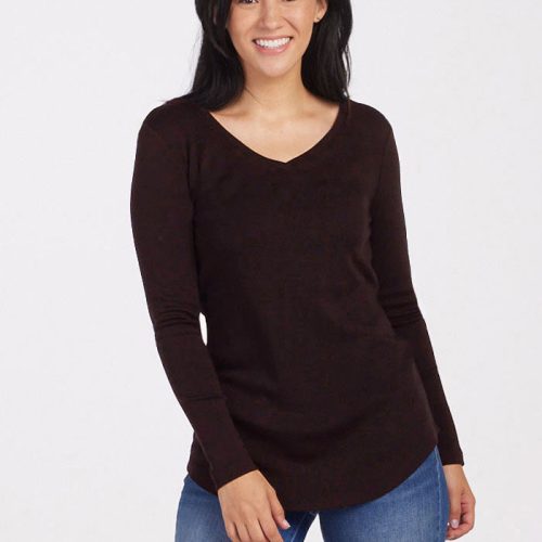 A smiling woman with long black hair, dressed in a dark French Roast Eva Tunic by Woolx and blue jeans, stands against a plain white background—an effortless winter wardrobe essential.