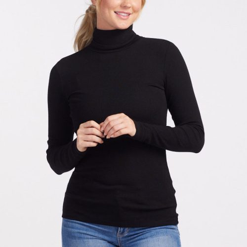 A person with blonde hair stands against a light background, wearing the Sage Ribbed Turtleneck in black by Woolx and blue jeans. The moisture-wicking fabric of the turtleneck ensures comfort. They have a relaxed expression and their hands are gently clasped in front.